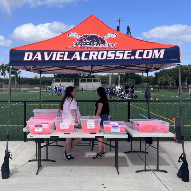 Women standing under a Custom designed canopy tent at a lacrosse tournament.